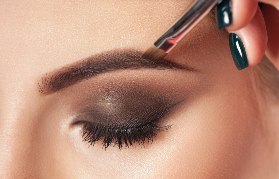 Make-up artist does eyebrow make-up to a woman with smoky eyes makeup. Beautiful thick eyebrows close up. Professional makeup and cosmetology skin care.